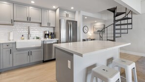 A modern kitchen with grey cabinets, a stainless steel refrigerator, a white marble island, and a black spiral staircase. - Ma'alaea Surf, D9 - Oceanfront Condo - remodeled two-bedroom, 2nd Floor (Kihei)