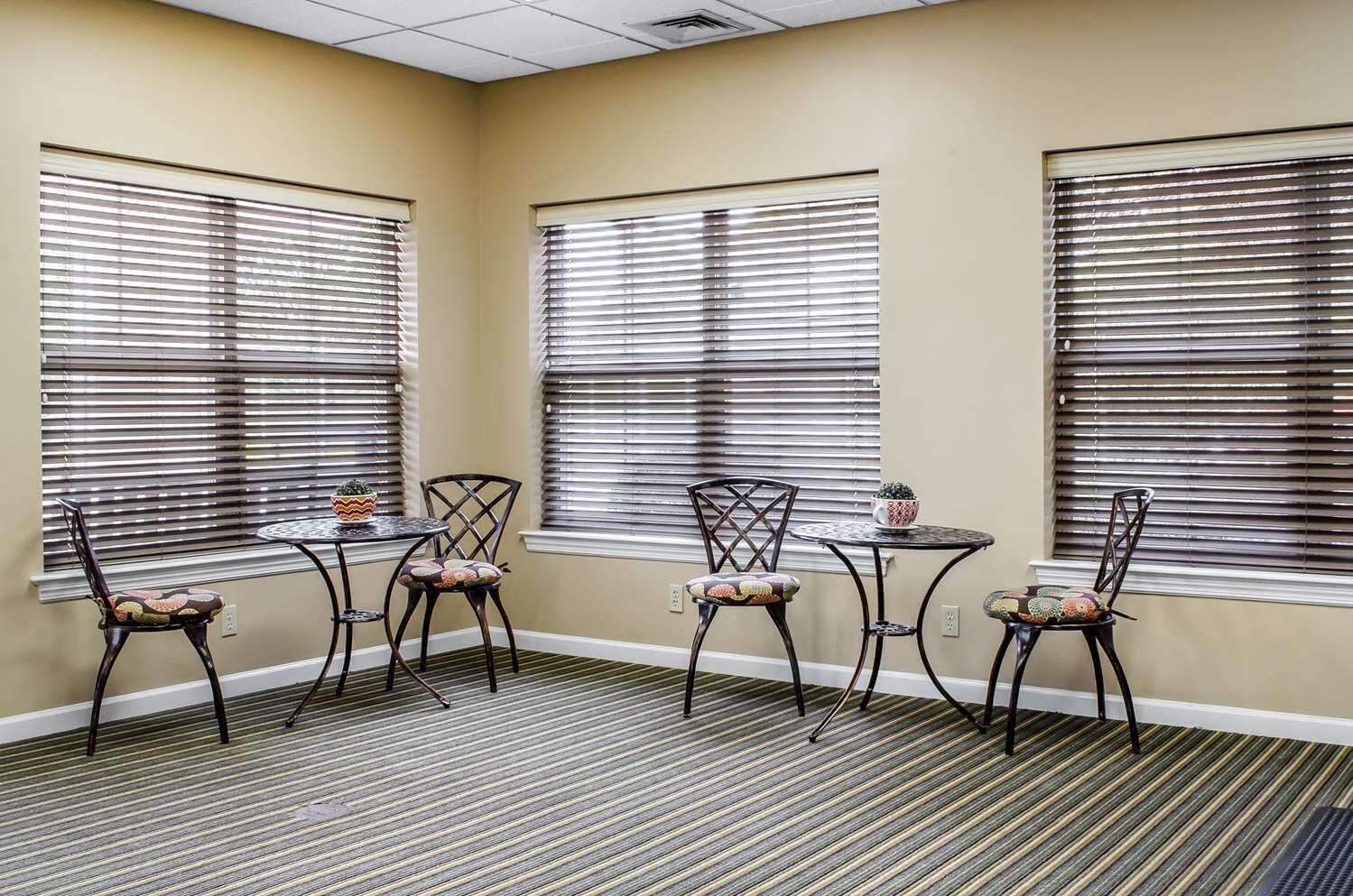 A room with three tables and four chairs, each with a cushion. The room has beige walls and striped carpet.