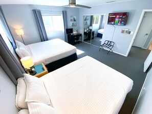 Ein Hotelzimmer mit zwei Betten, einem Schreibtisch, einem Sessel, einem Fernseher und einem Spiegel.