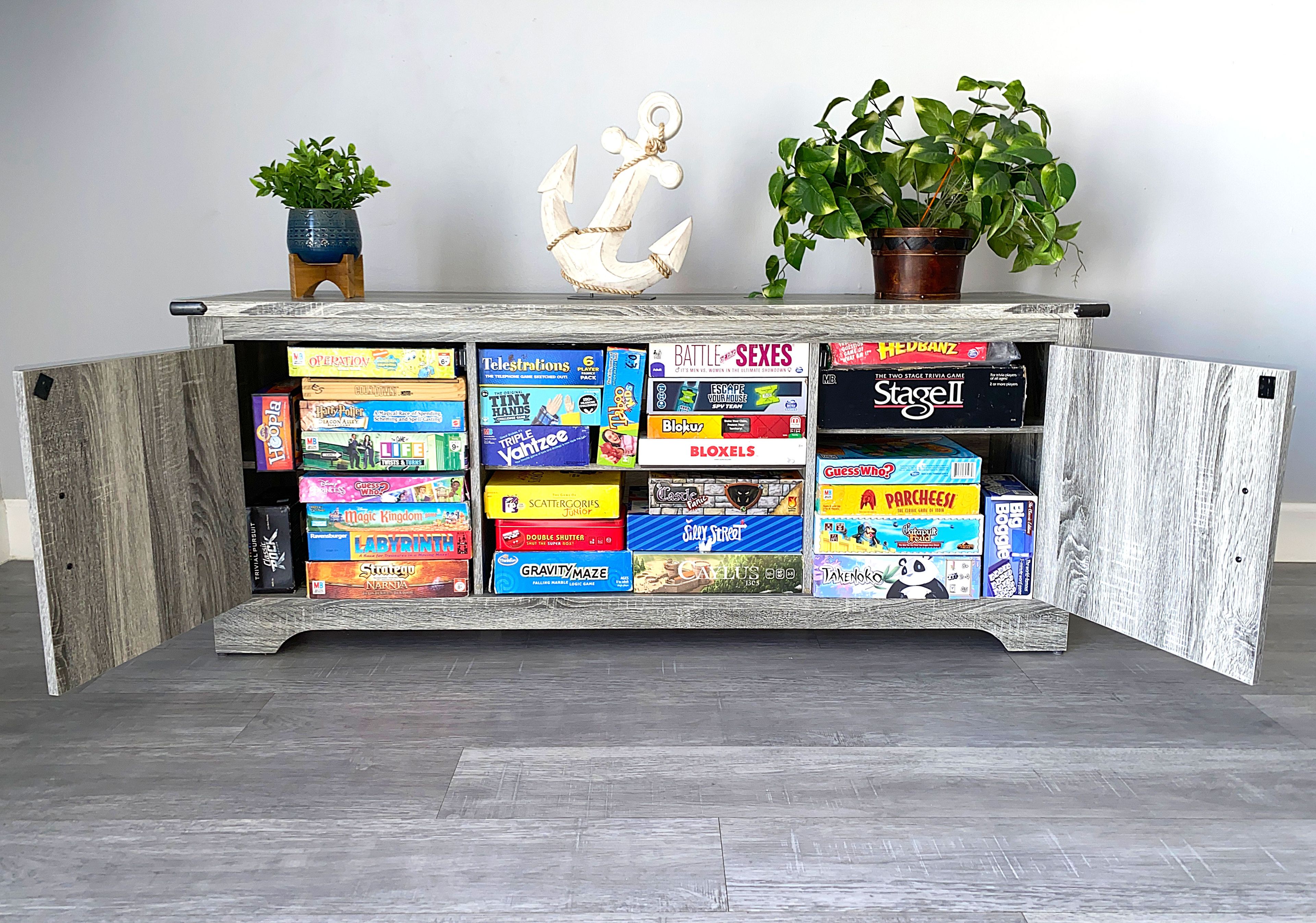 Een houten kastje met diverse gezelschapsspellen en twee planten in potten.