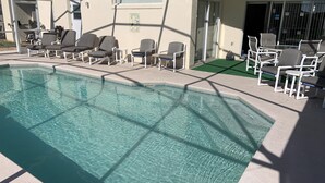 A swimming pool with clear water, surrounded by lounge chairs and a building with a covered patio area. - Summer State Of Mind - NEW Pool Home (Haines City)