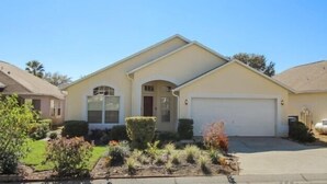 A single-story house with a garage, a front yard with various plants, and a clear blue sky. - Summer State Of Mind - NEW Pool Home (Haines City)