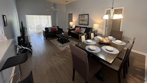 A modern living room with a dining area, featuring a large dining table, chairs, a sofa, and a ceiling fan. - Just Keep Swimming - NEW Pool Home (Davenport)