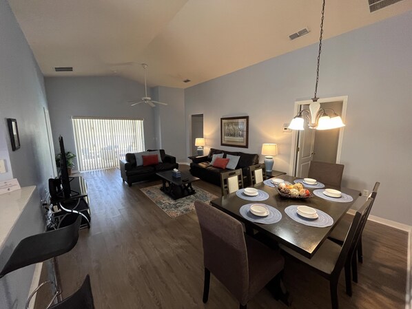 Un salon moderne avec un coin repas, comprenant une grande table à manger, des chaises, un canapé et un ventilateur de plafond.