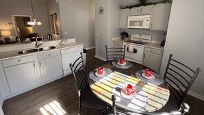 A compact kitchen with white cabinets, a microwave, and a stove. There is a dining table with four chairs and red cups. - Just Keep Swimming - NEW Pool Home (Davenport)