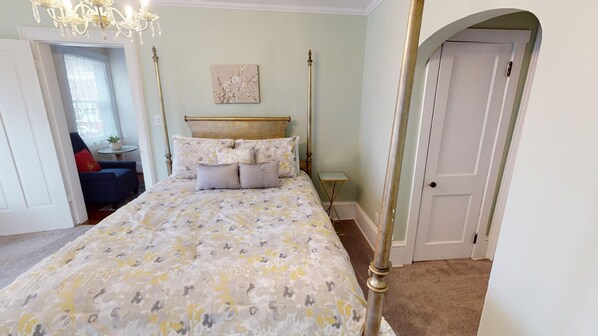 A bedroom with a large bed, a chandelier, a small table, and a door.