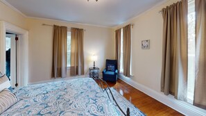 A spacious bedroom with a large bed, a chair, and curtains on the windows.