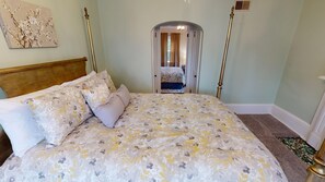 A bedroom with a bed, a nightstand, a lamp, and a door leading to another room.
