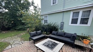 Un patio con un sofá modular, una mesa de vidrio y un camino de ladrillo.