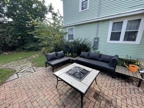A patio with a sectional sofa, a table with a glass top, and a brick pathway.