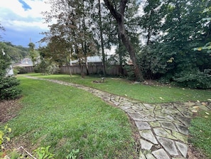 A backyard with a stone pathway, green grass, and trees.