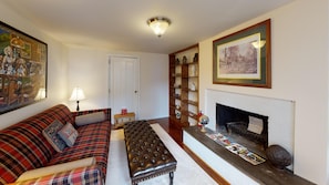 A living room with a plaid sofa, a leather ottoman, a fireplace, and a bookshelf. - Beautiful 1850 Inn close to Nelsonville Town Square, near Hocking Hills (Nelsonville)
