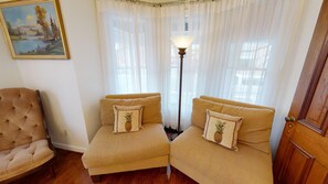 A room with two beige sofas, a wooden chair, a floor lamp, and a painting on the wall.