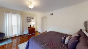 A bedroom with a bed, a dresser, a lamp, a door, and a window with curtains.