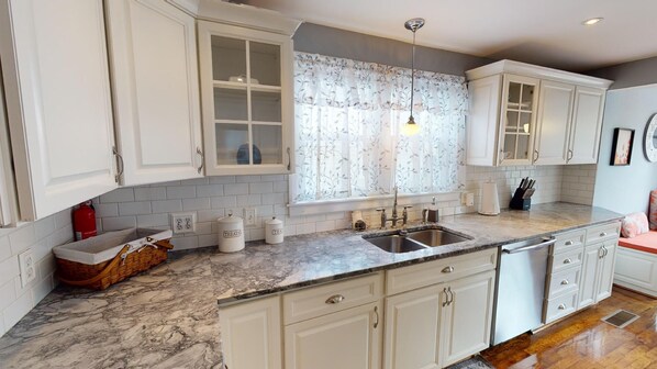 A kitchen with white cabinets, a marble countertop, a sink, and a window with floral curtains.