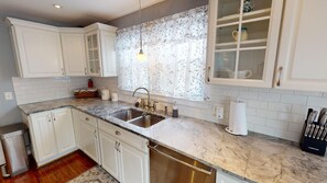 A kitchen with white cabinets, a marble countertop, a stainless steel sink, and a window with floral curtains.