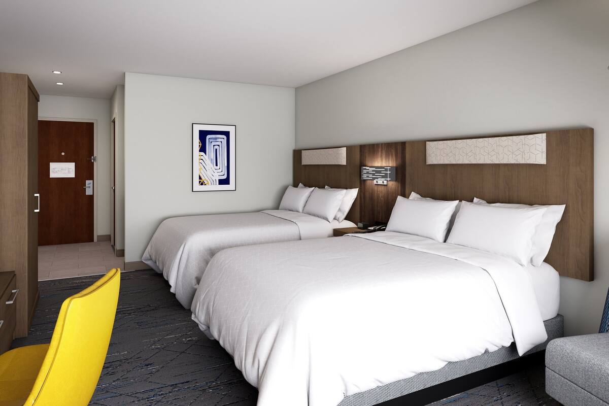 A hotel room with two beds, a wooden headboard, a desk, a chair, and a framed picture on the wall.