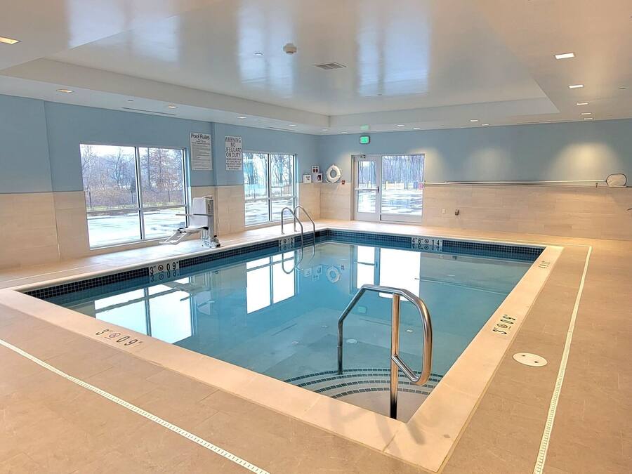 Una amplia piscina interior con normas claras y señalización de capacidad, rodeada de ventanas y un suelo de baldosas.