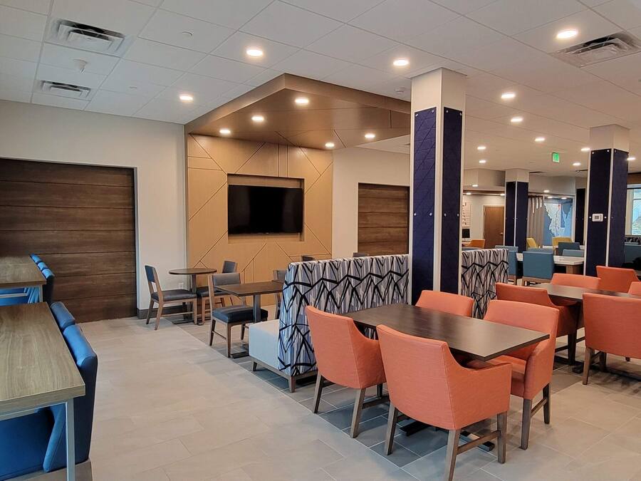 Um restaurante moderno com mesas altas e cadeiras laranja, uma grande tela de televisão e um painel de parede em madeira.