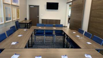 A conference room with a long table, blue chairs, and a TV mounted on the wall.