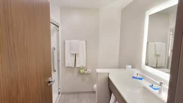Un baño con puerta de madera, un lavamanos blanco con espejo y dos toallas blancas colgadas en la pared.