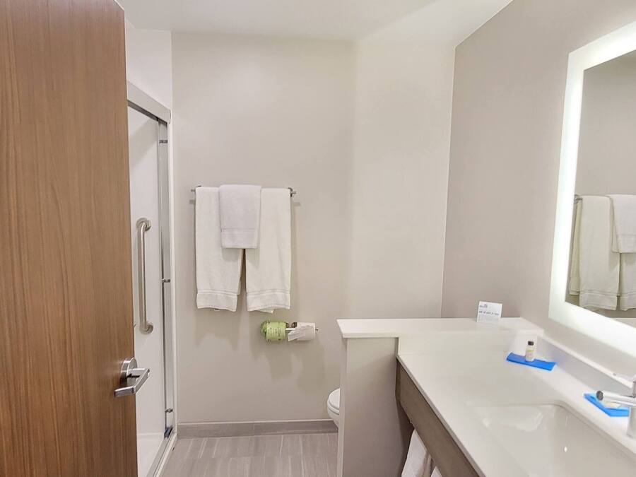 A bathroom with a wooden door, a white sink with a mirror, and two white towels hanging on the wall.