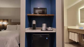 Une chambre d’hôtel équipée d’un lit, d’un mini-bar, d’une machine à café, d’une poubelle et d’une salle de bain avec un miroir et un porte-serviettes.