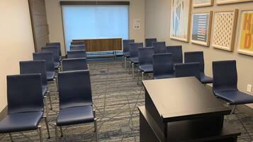 A conference room with rows of blue chairs, a projector screen, and framed artwork on the walls.
