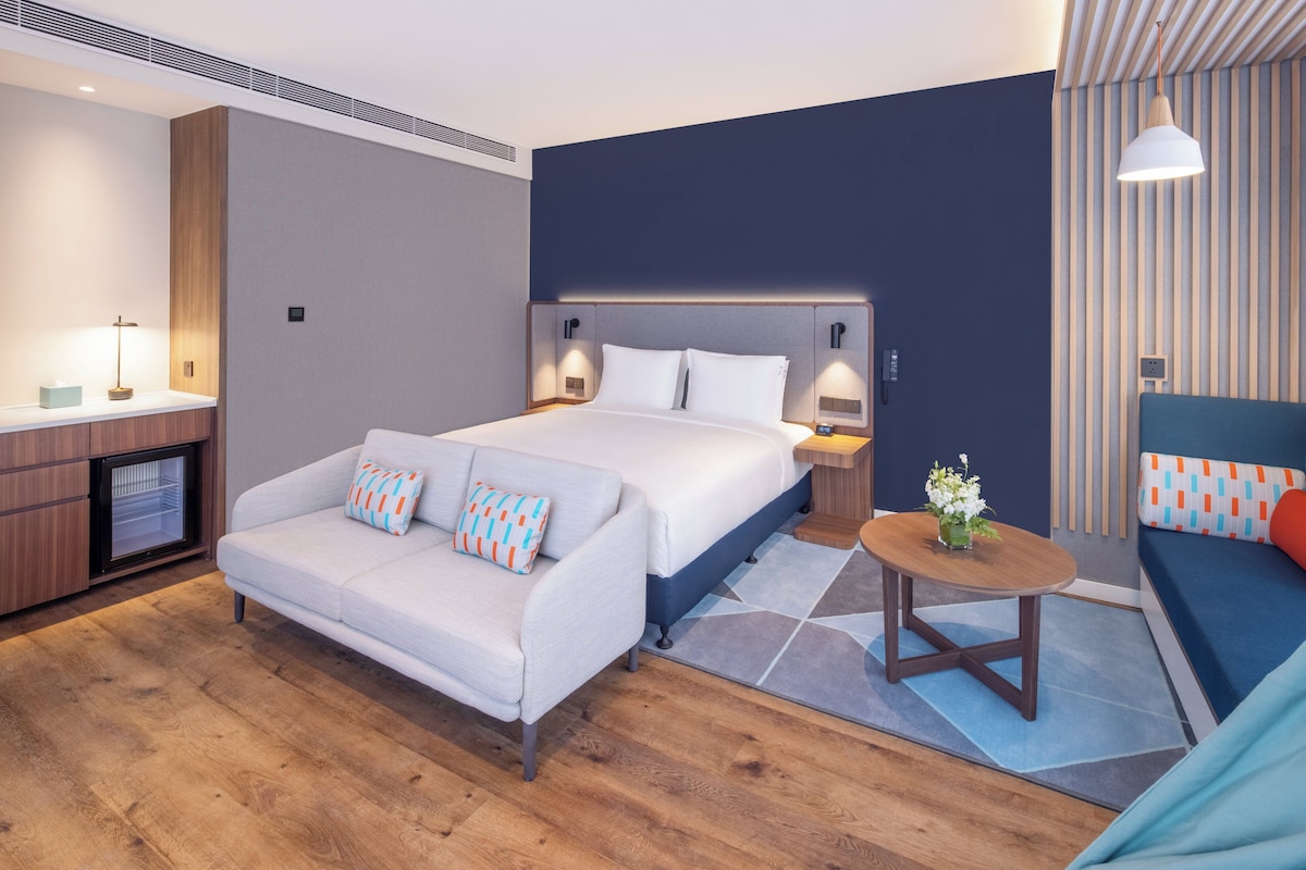 Une chambre d’hôtel moderne équipée d’un lit, d’un canapé, d’une petite table et d’un mini-bar.