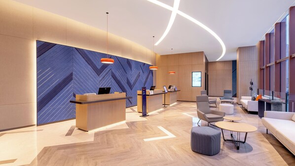 A modern hotel lobby with a reception desk, seating area, and a large blue patterned wall.