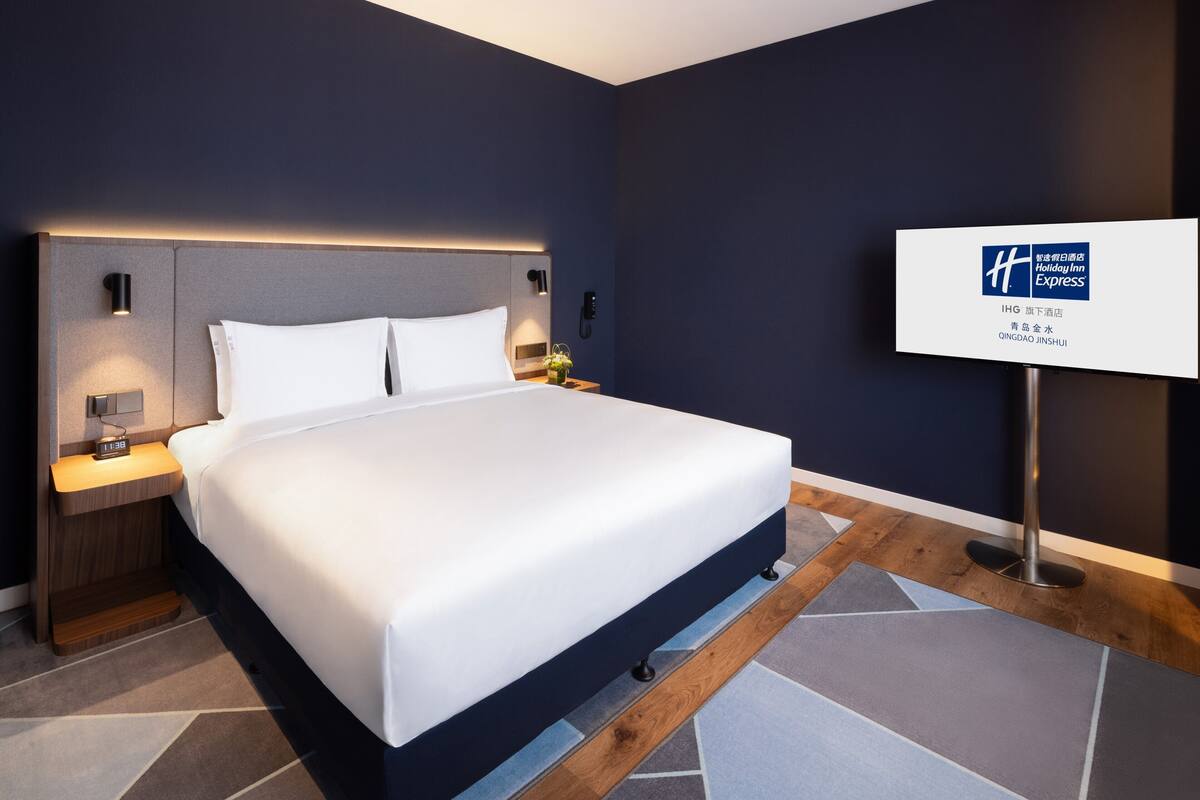 A modern hotel room with a large bed, bedside tables with lamps, a nightstand, and a sign indicating it's a Holiday Inn Express.