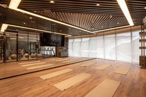 Una palestra moderna con pavimento in legno, tappetini da ginnastica, uno specchio grande e uno schermo TV.
