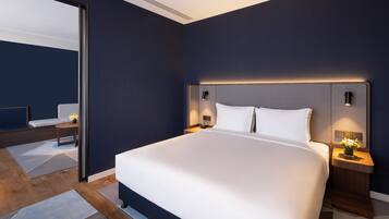 A modern hotel room with a large bed, bedside tables with lamps, a mirror, and a view of the adjacent room.