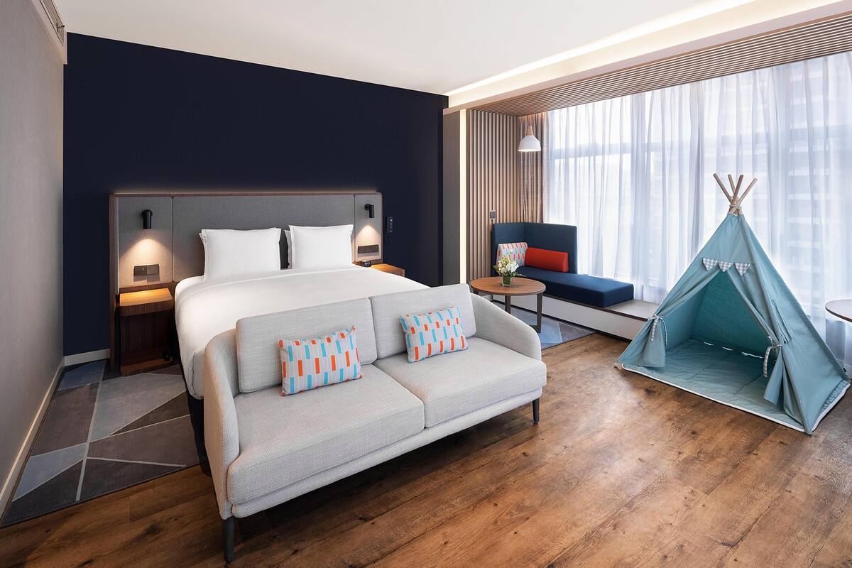 A modern hotel room with a bed, sofa, and a teepee.