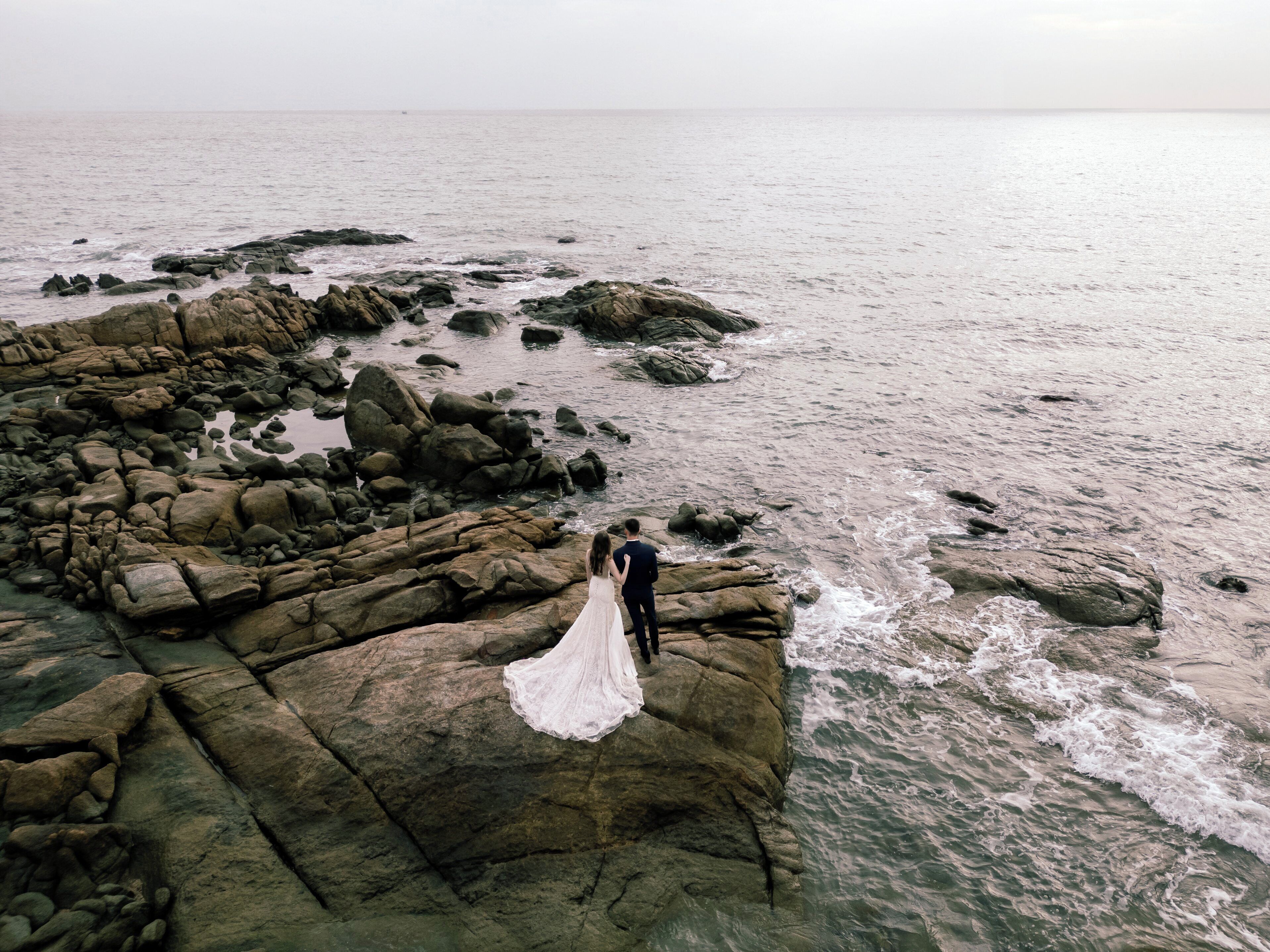 A rocky shoreline with a couple standing on a large rock formation.