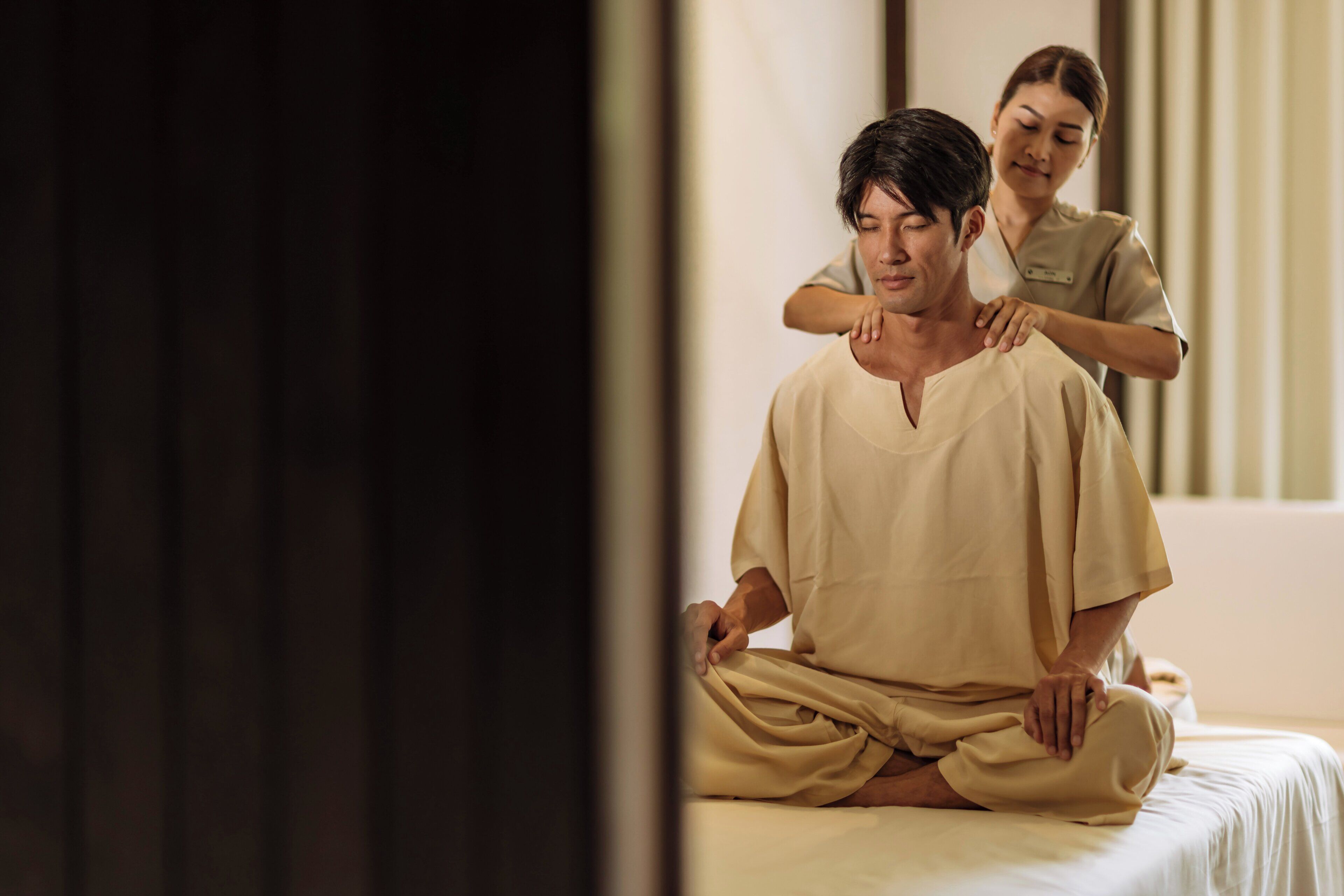 A person receiving a massage in a room with a bed and a window.