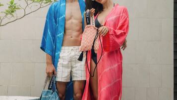 A man and a woman standing in front of a tiled wall, holding a striped bag and a small handbag.