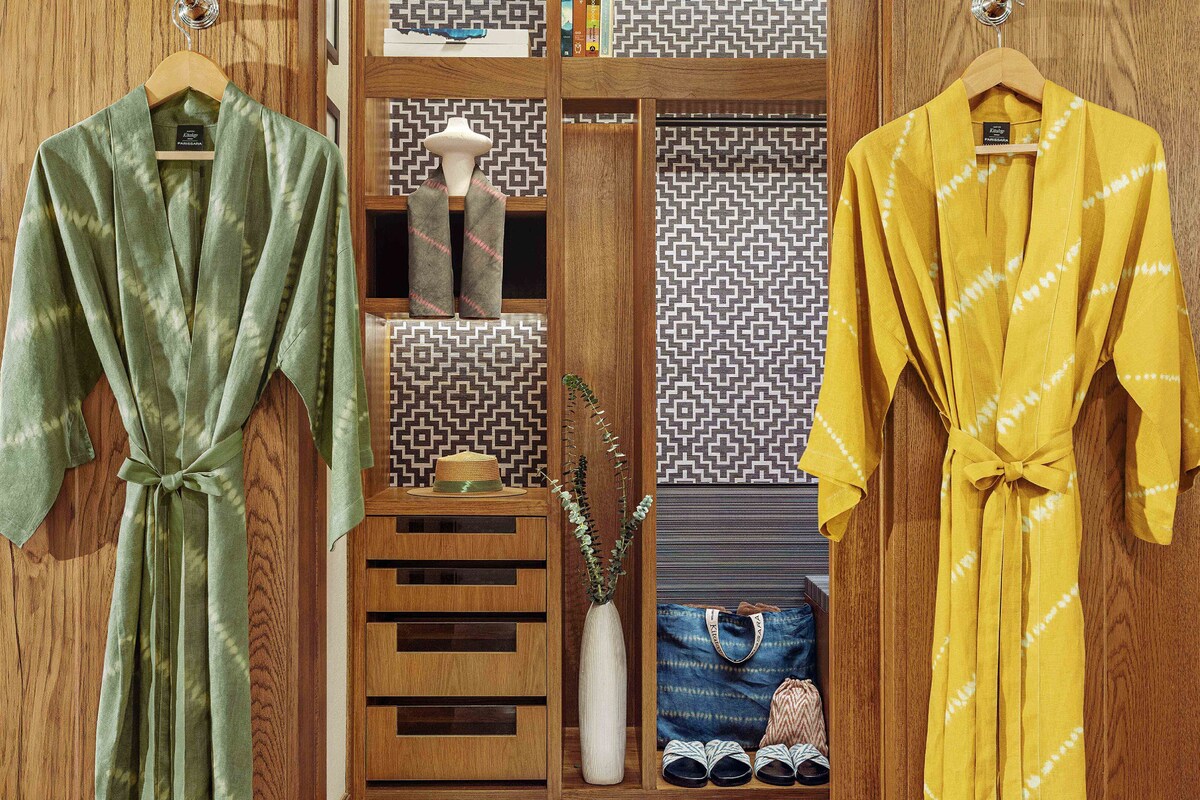 A wooden wardrobe with two robes hanging on hangers, a vase with a plant, and a patterned wall.