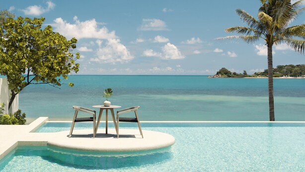 A pool with two chairs and a table, overlooking a clear blue sea and a tropical island. - Kimpton Kitalay Samui by IHG (Koh Samui)