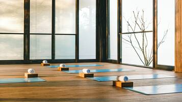 A yoga studio with wooden floors and large windows, featuring yoga mats and blocks.