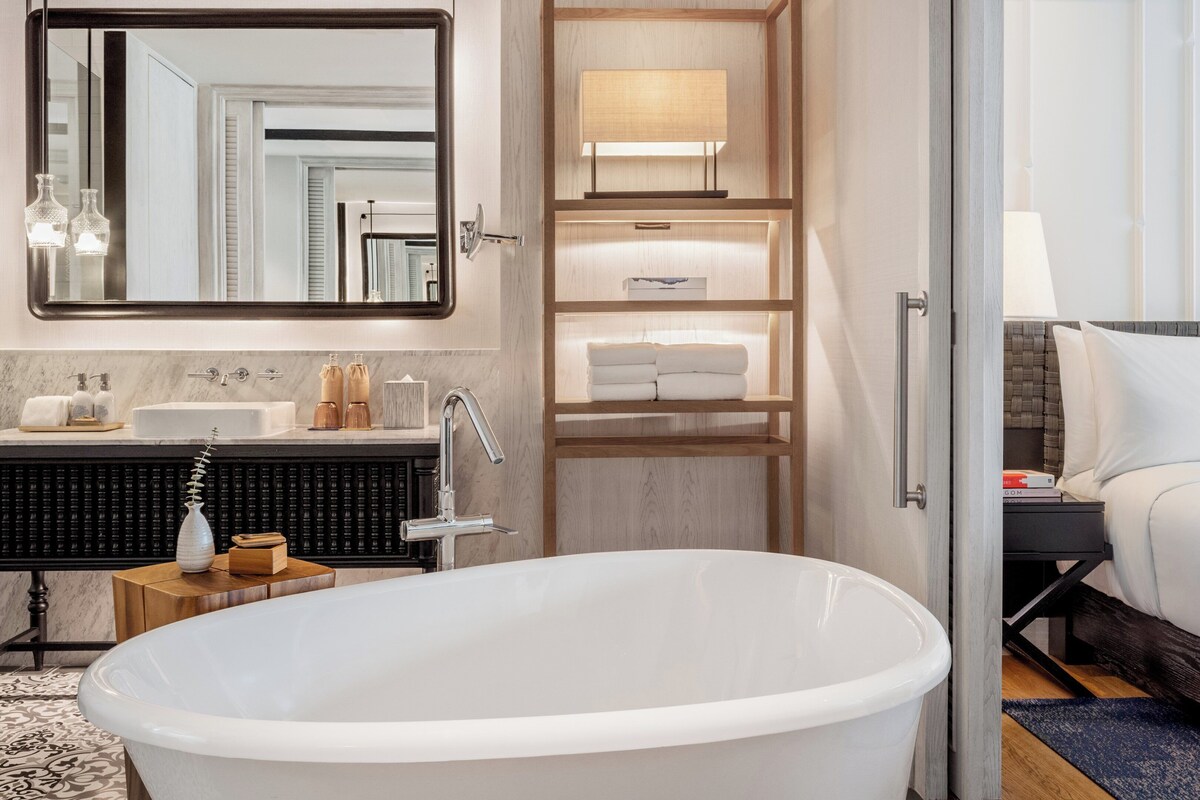 A modern bathroom with a freestanding bathtub, a vanity with a mirror, and a shelf with towels.
