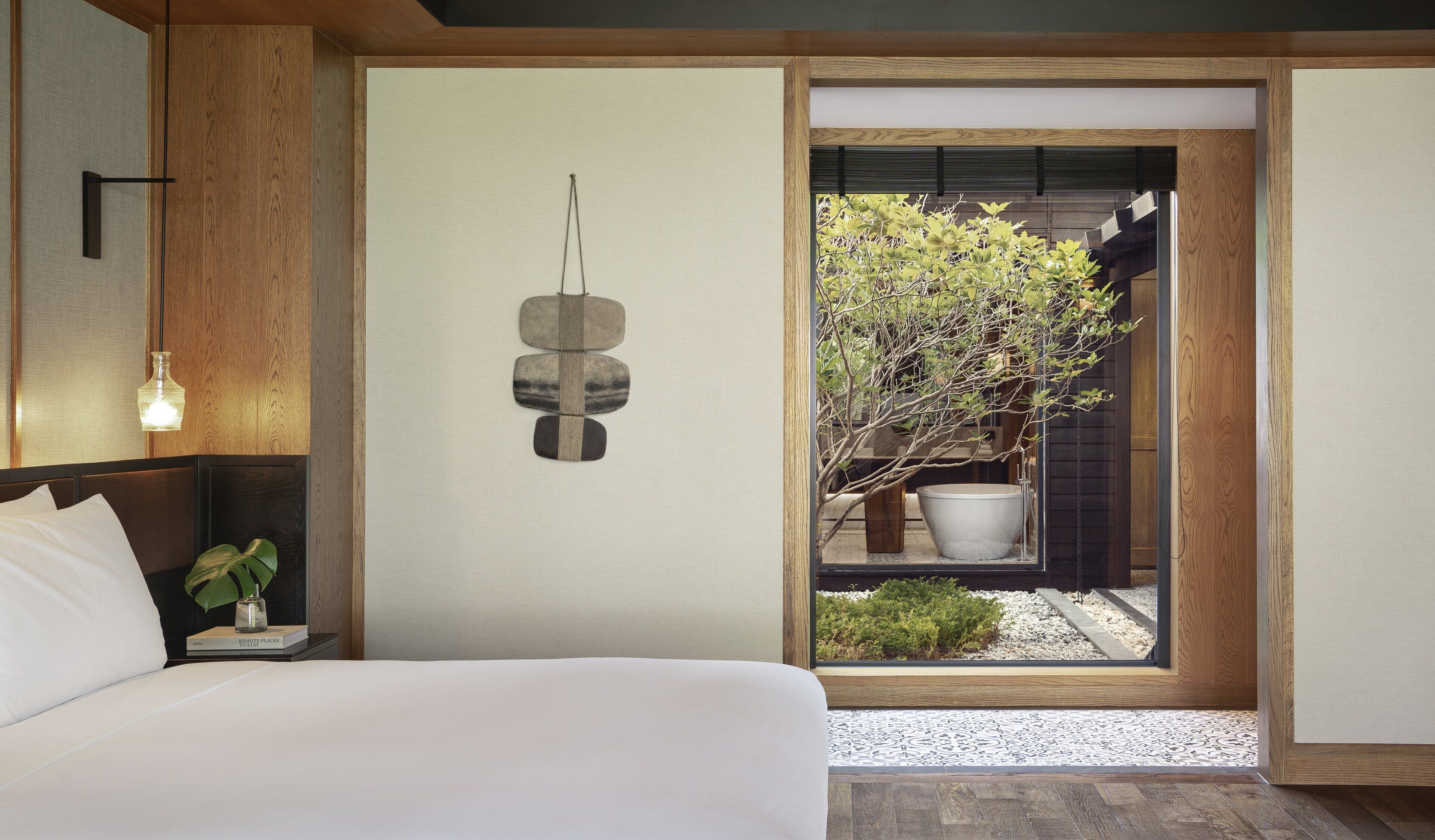 Un dormitorio moderno con cama, mesita de noche, lámpara y vistas a un jardín a través de una puerta corredera.