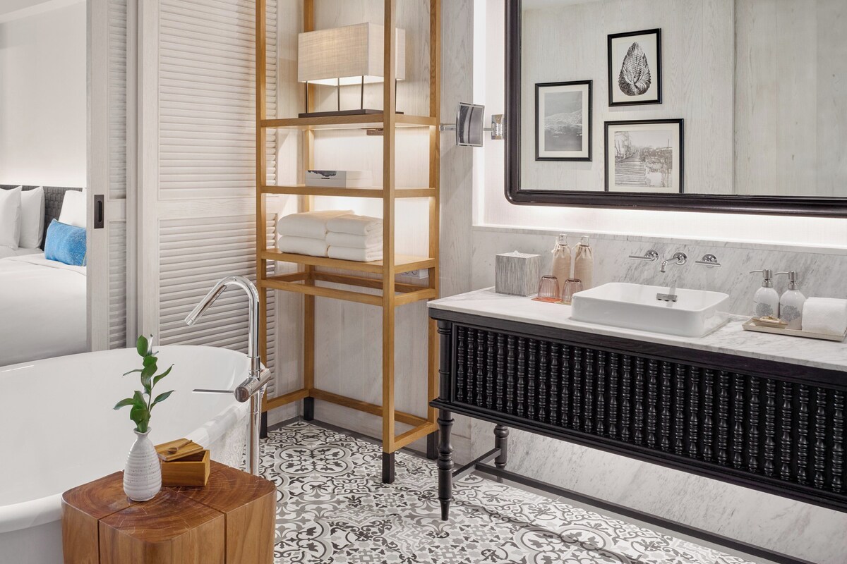A modern bathroom with a freestanding bathtub, a wooden vanity with a large mirror, and a tiled floor.