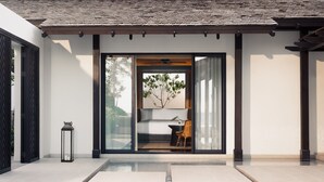 A modern building with a glass door entrance, a small indoor seating area with a table and chair, and a lantern on the ground. - Kimpton Kitalay Samui by IHG (Koh Samui)