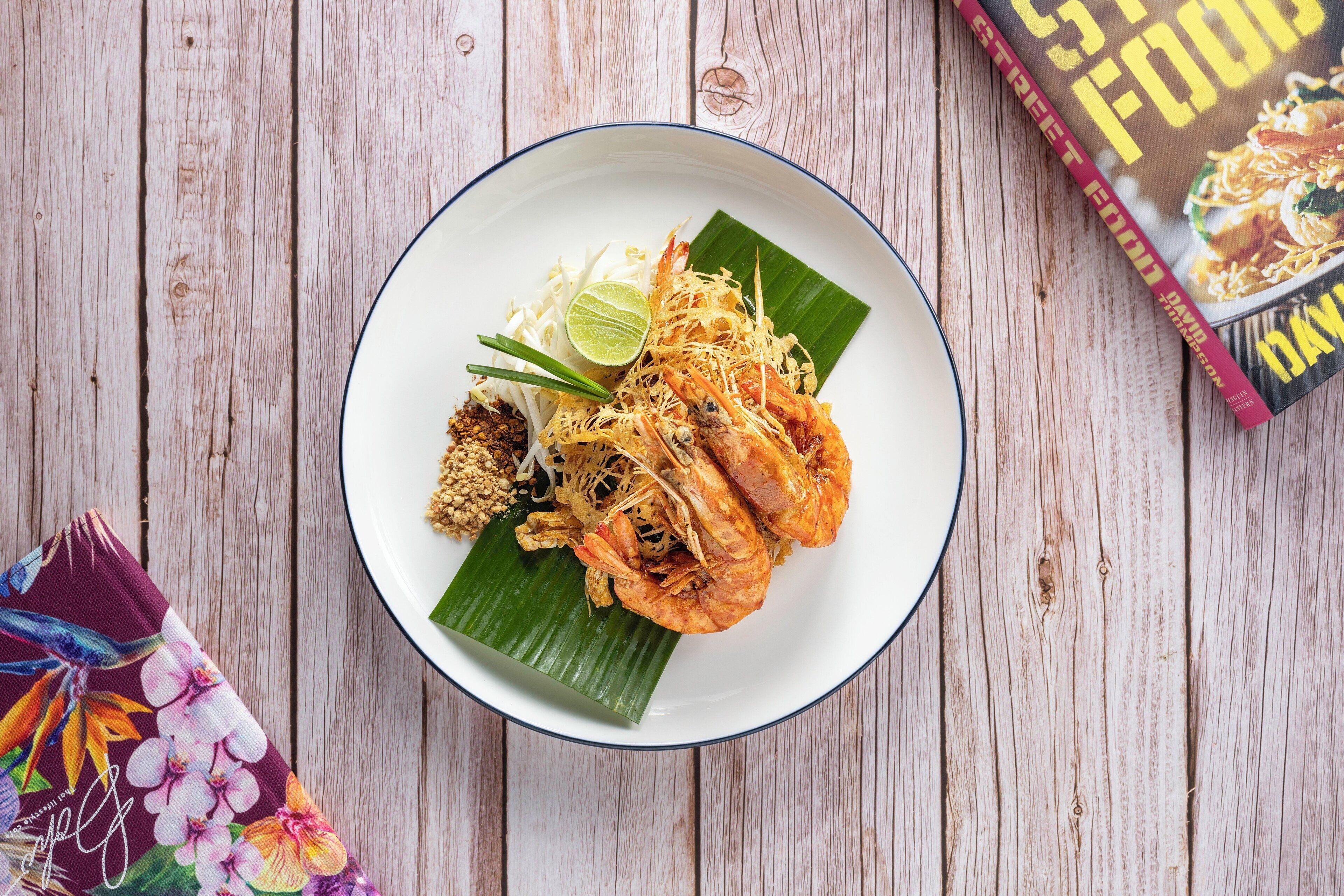 A plate of food with shrimp, noodles, and lime on a wooden table.
