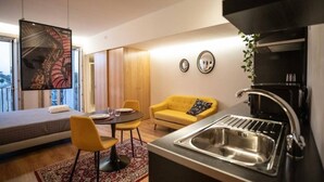 A modern living room with a sofa, a dining table, and a kitchen area with a sink and coffee machine. - Lemago Porto Apartments - POVEIROS 2B (Porto)