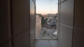 A view from a window with a tiled floor, looking out onto a street with buildings and a flag. - Lemago Porto Apartments - POVEIROS 2B (Porto)