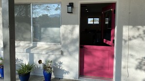 A house with a pink door, a window with blinds, and two potted plants on the porch.
