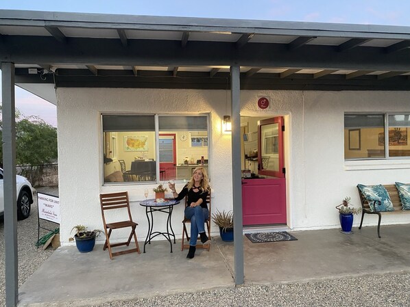 A building with a covered patio, a dining area with a table and chairs, and a red door.
