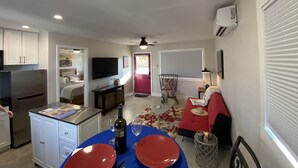 A compact living space with a kitchenette, a dining area with red plates, a TV mounted on the wall, and a red door leading to another room.
